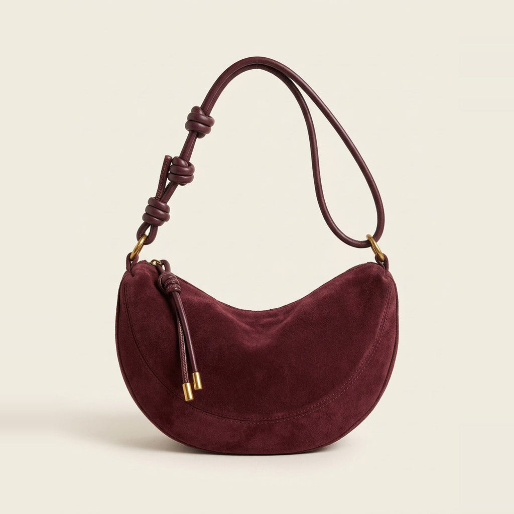 Hero view of the crescent shoulder bag in burgundy resting on a book.