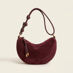 Hero view of the crescent shoulder bag in burgundy resting on a book.