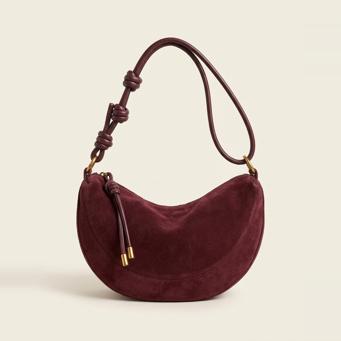 Hero view of the crescent shoulder bag in burgundy resting on a book.