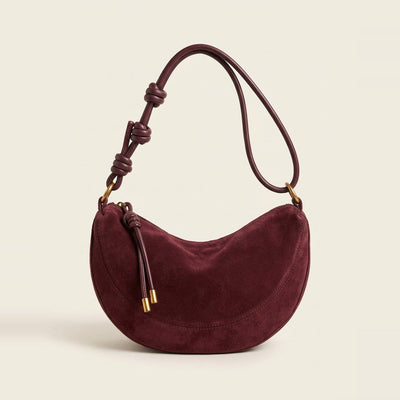 Hero view of the crescent shoulder bag in burgundy resting on a book.