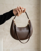Side profile of the crescent shoulder bag in chocolate held by the shoulder strap