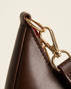 Macro close-up of the metal clip hardware and stitching on the crescent shoulder bag in chocolate
