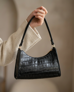Croc-embossed baguette shoulder bag in black worn under the arm with a tailored blazer.