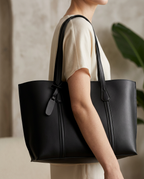 Black faux leather tote bag held at the shoulder