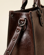 Close-up of glazed chocolate surface, contrast topstitching, and handle hardware
