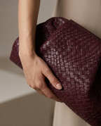 Gathered upper frame of the woven clutch in burgundy held in hand