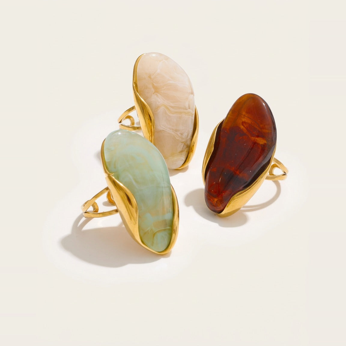 Three marbled organic stone cocktail rings in Cognac, Cream, and Light Olive.