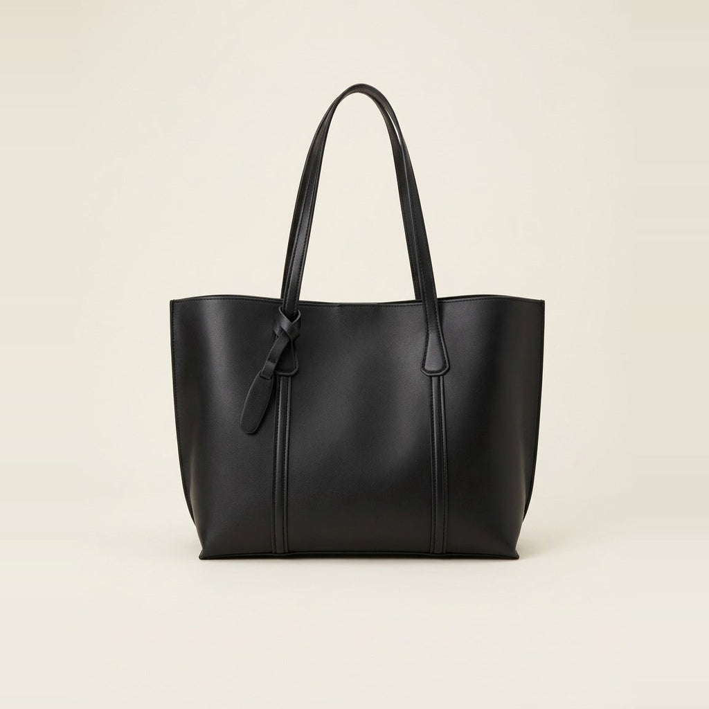 Black minimalist faux leather tote bag sitting upright on a grey carpet