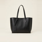 Black minimalist faux leather tote bag sitting upright on a grey carpet