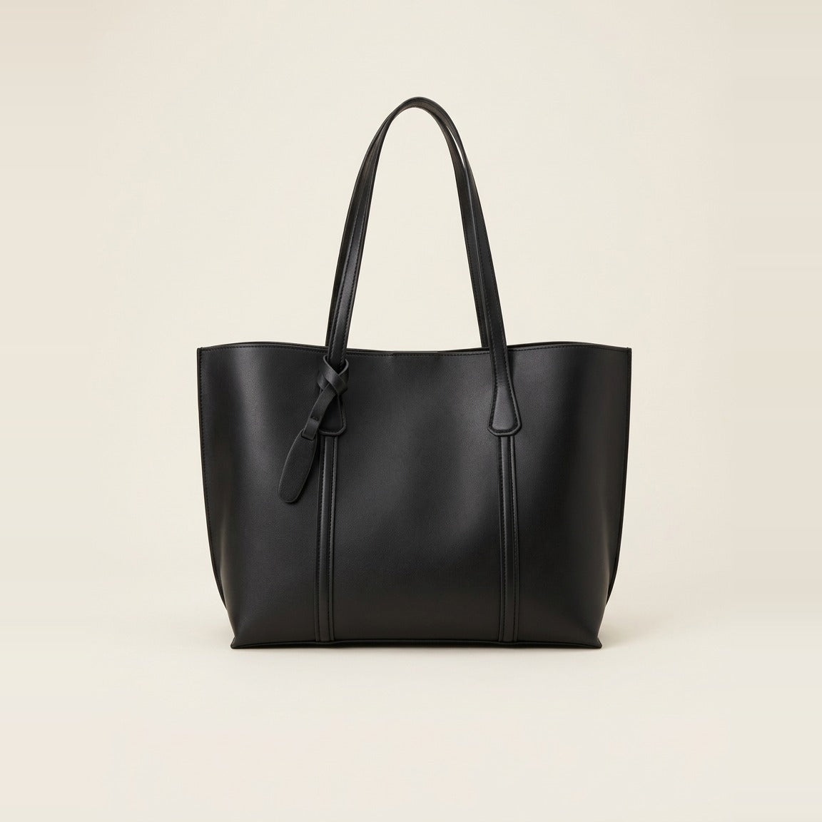 Black minimalist faux leather tote bag sitting upright on a grey carpet