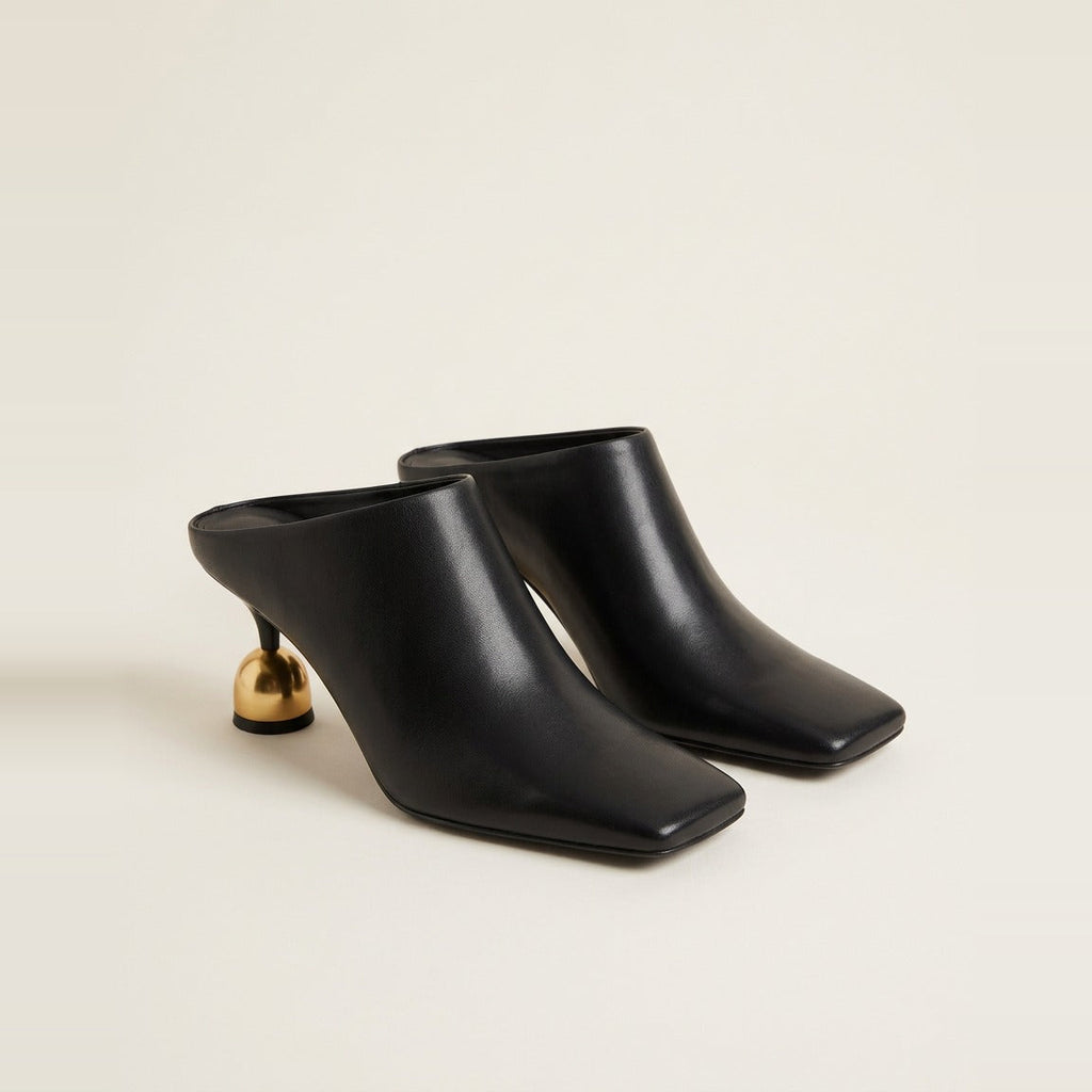 Black sculptural heel mule on a glass surface.