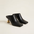 Black sculptural heel mule on a glass surface.