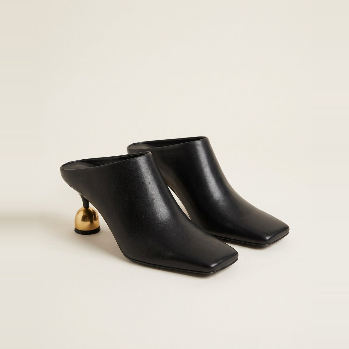 Black sculptural heel mule on a glass surface.