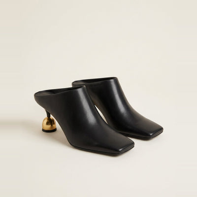 Black sculptural heel mule on a glass surface.