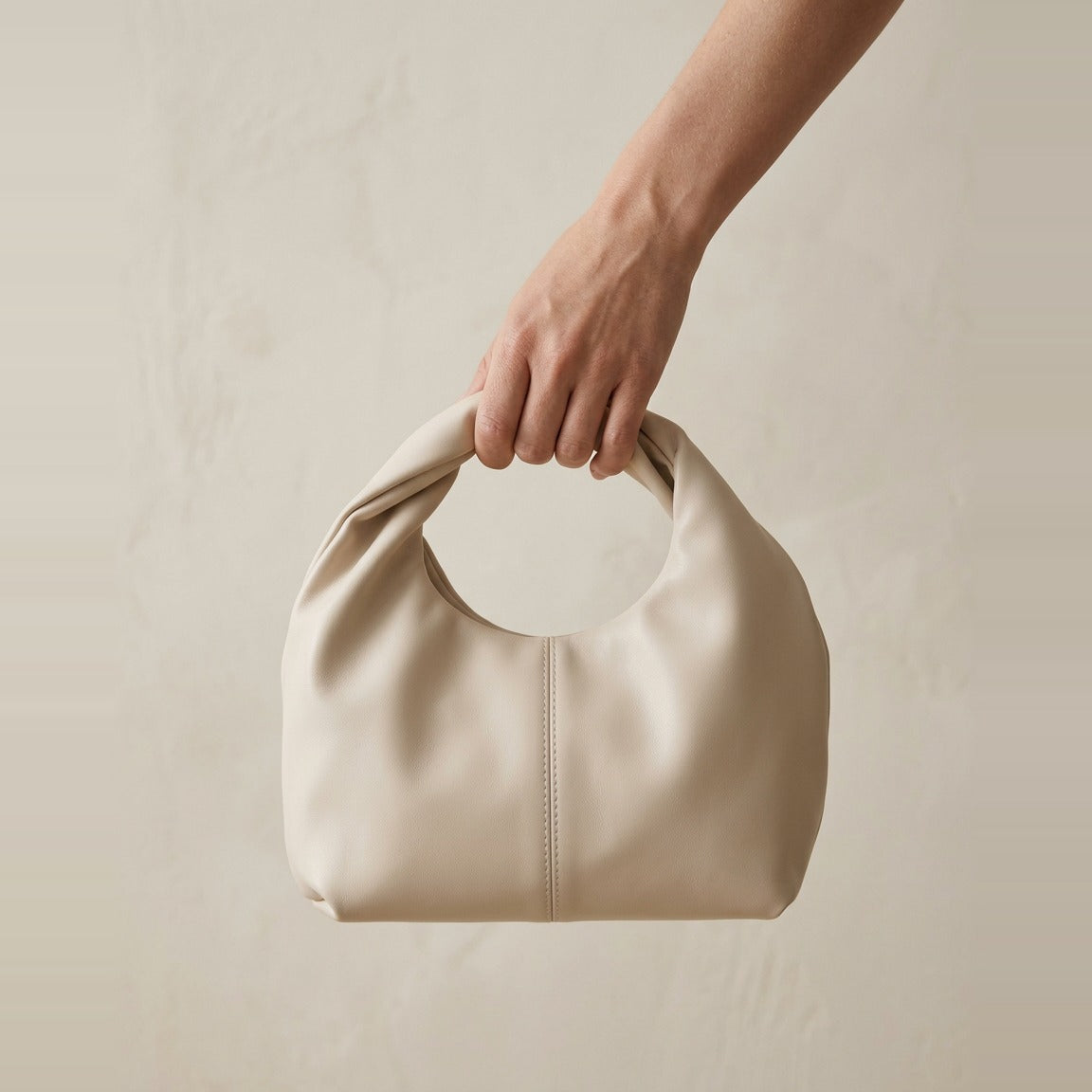 Side profile of the twisted handle hobo bag in cream showing the gathered fold